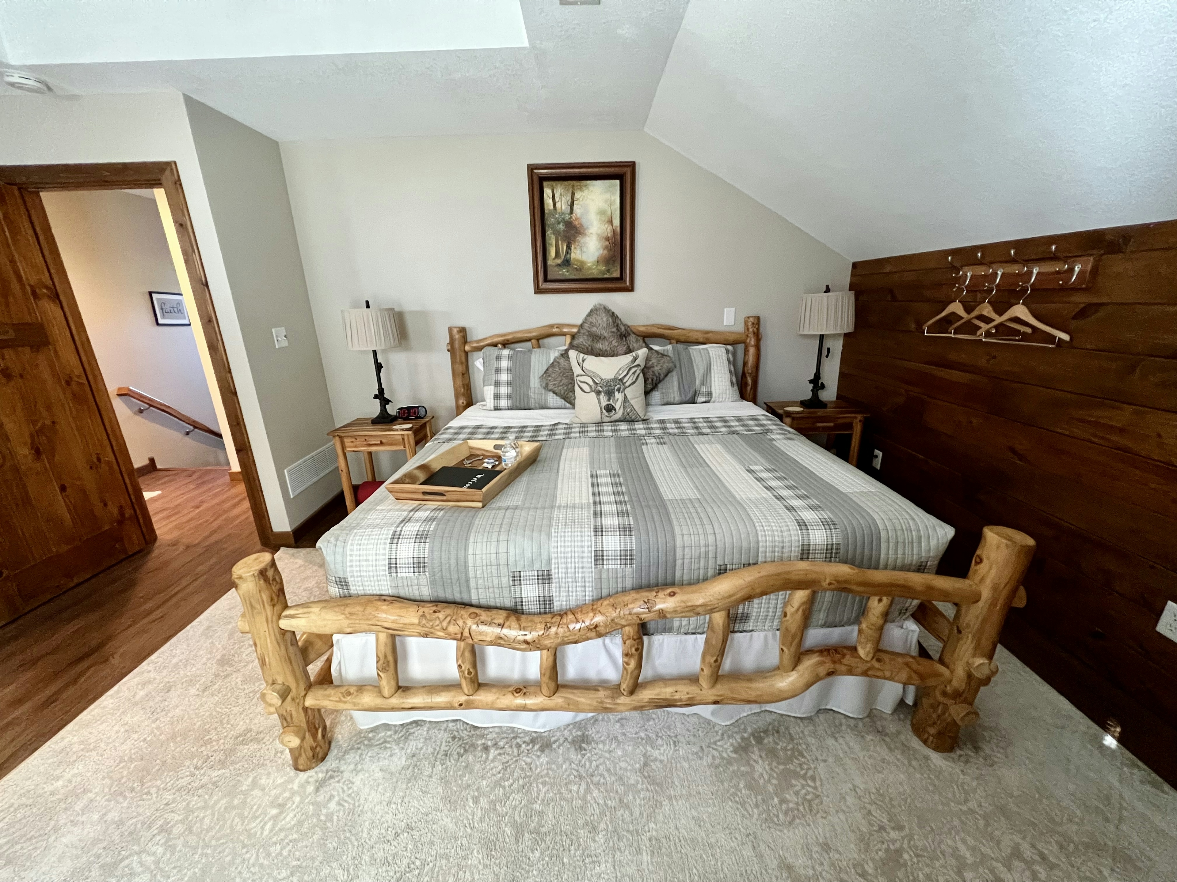 king size log bed with grey and white quilt, two side tables with lamps and picture above bed