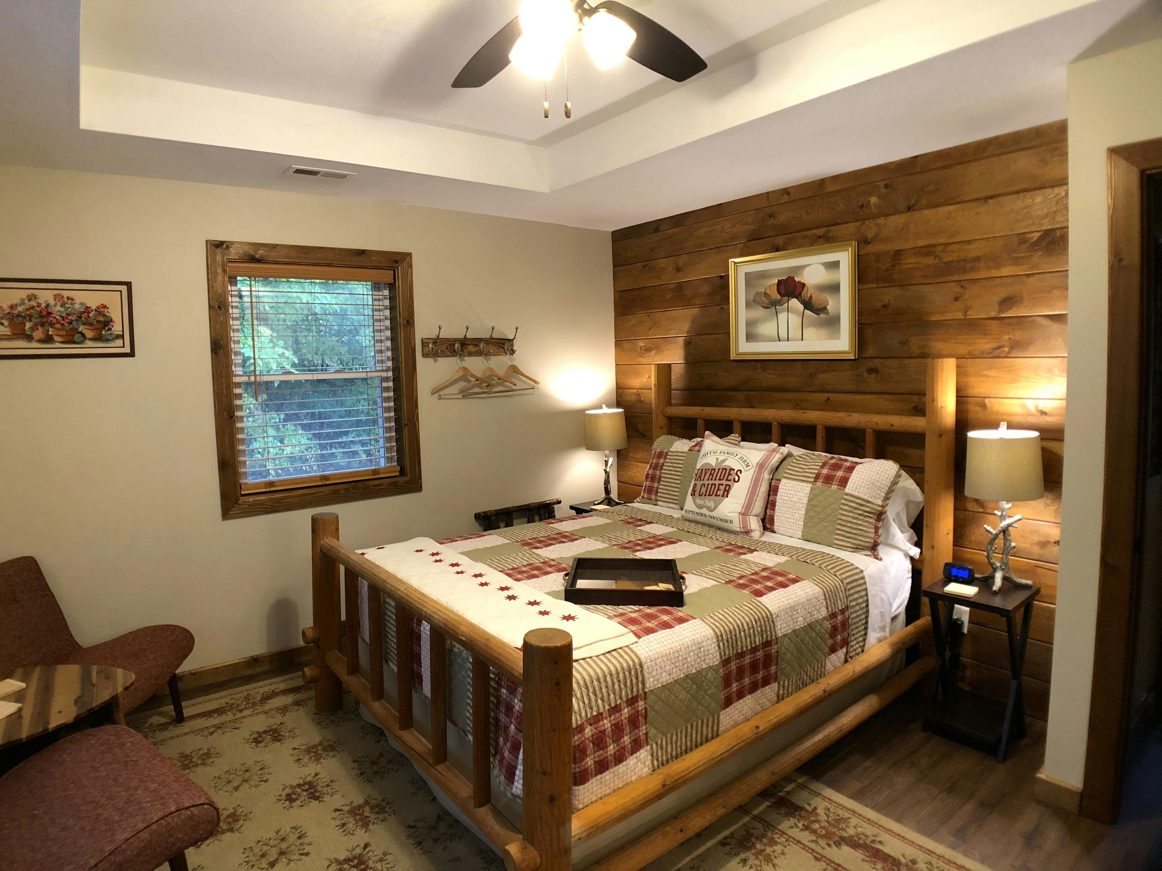 Log style bed with red and white country quilt, ceiling fan, wooden accent wall behind the bed