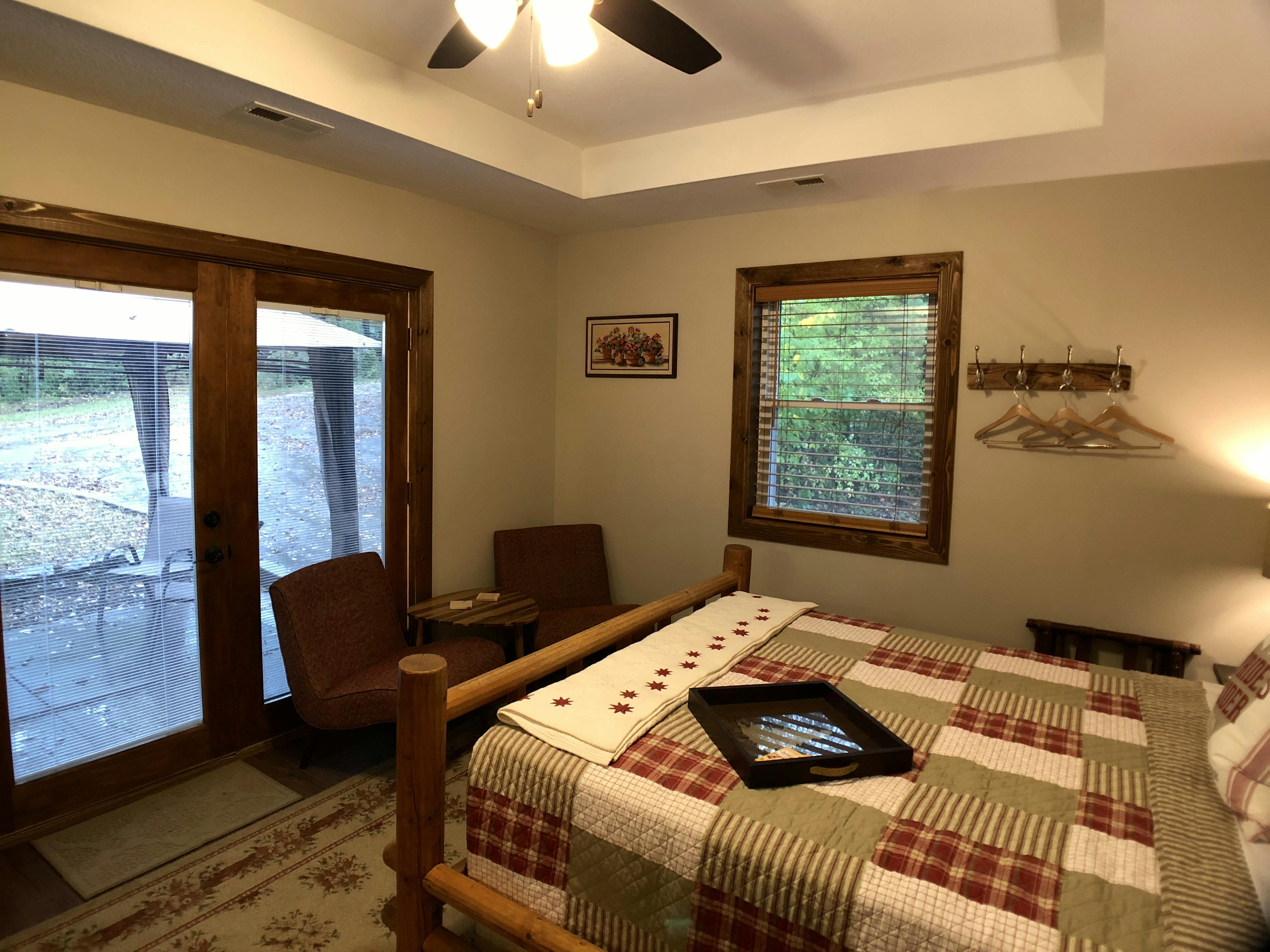 log style bed with red, tan and white country quilt, two red chairs and french doors leading outside