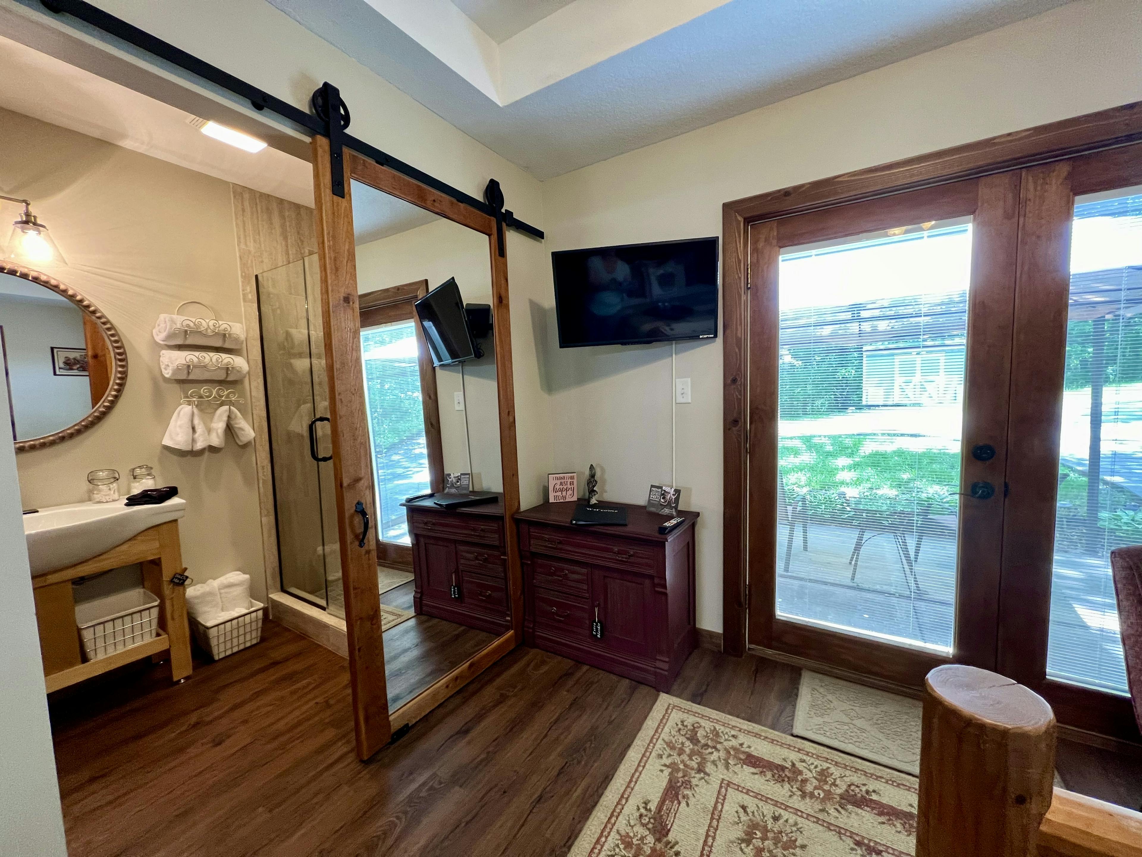 barn style mirrored door open to bathroom, small dresser and wall mounted tv