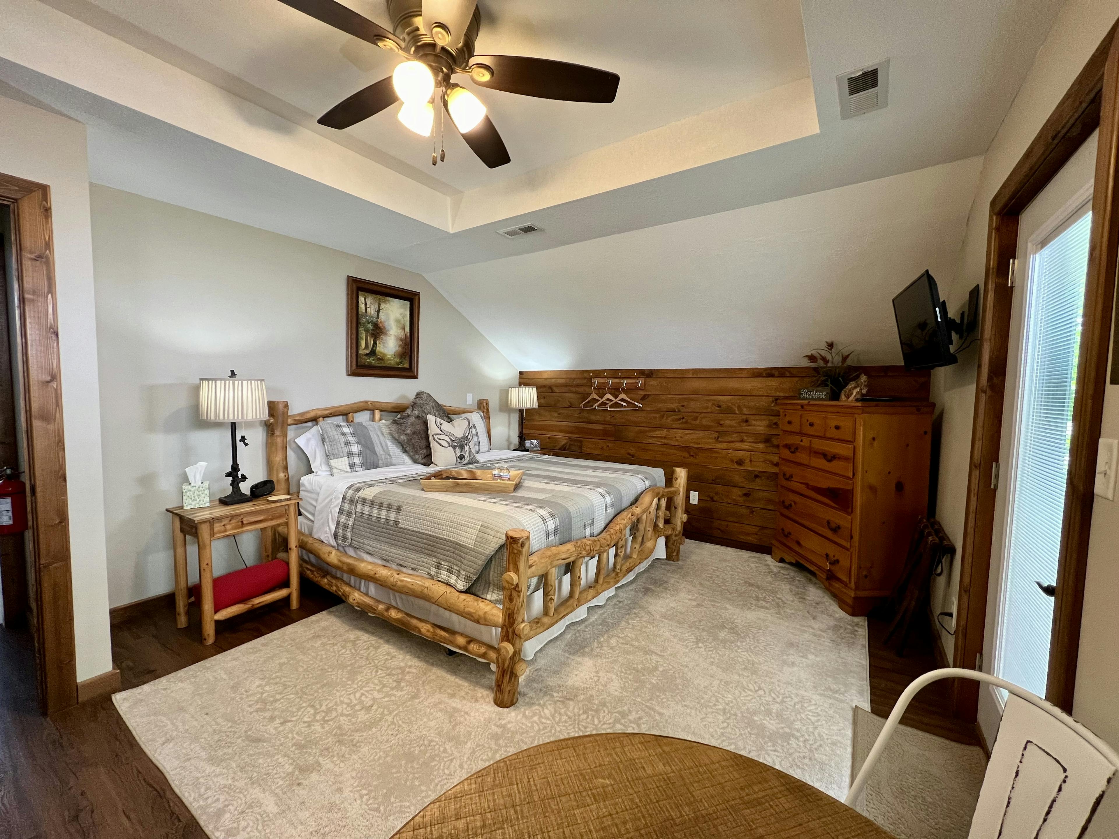 Log style bed with grey and white quilt, wooden tall dresser, wall mounted tv, exterior door