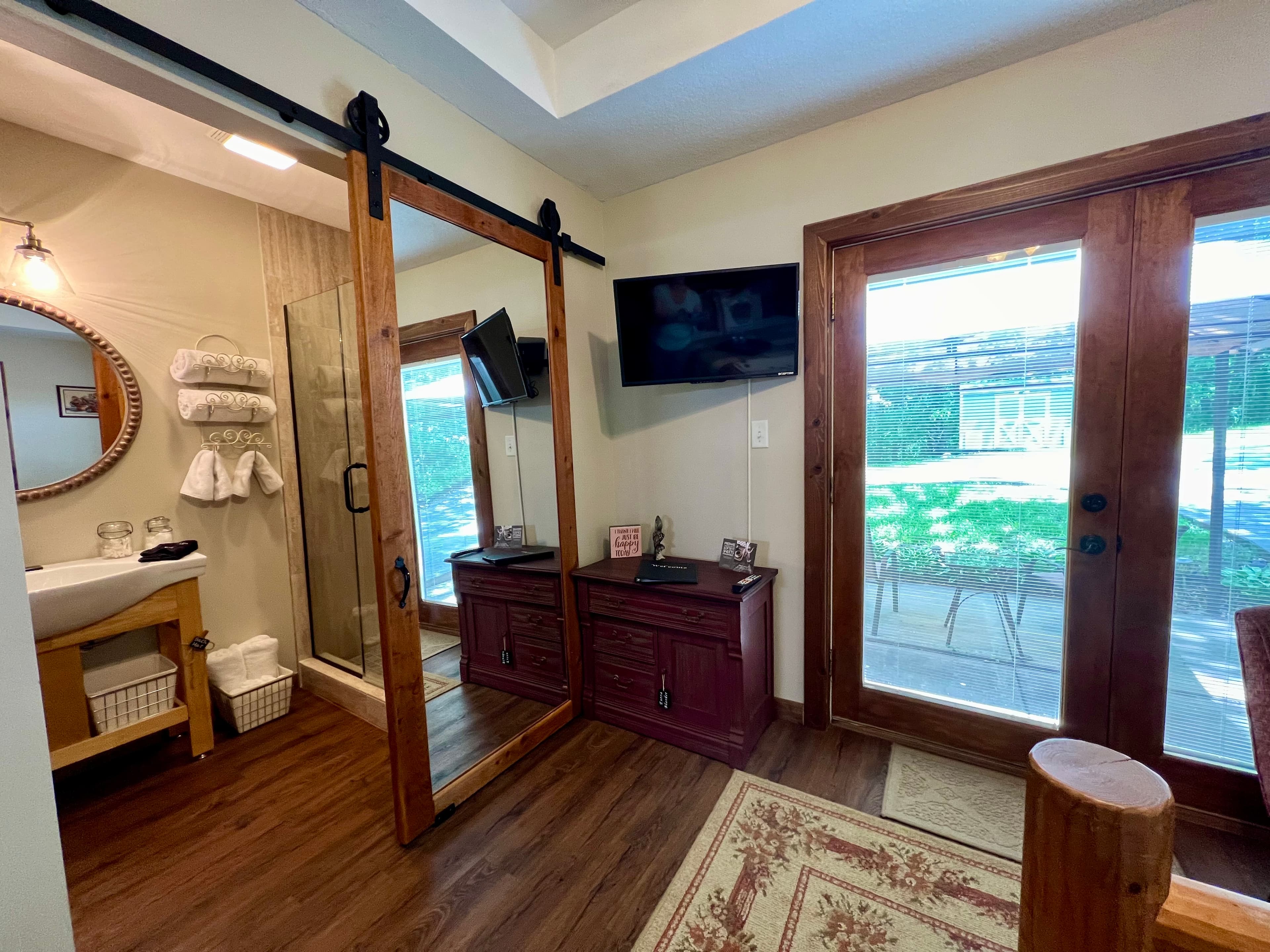 barn style mirrored door open to bathroom, small dresser and wall mounted tv